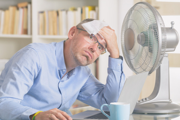 man sweating in front of a fan on a laptop looking for air conditioning systems